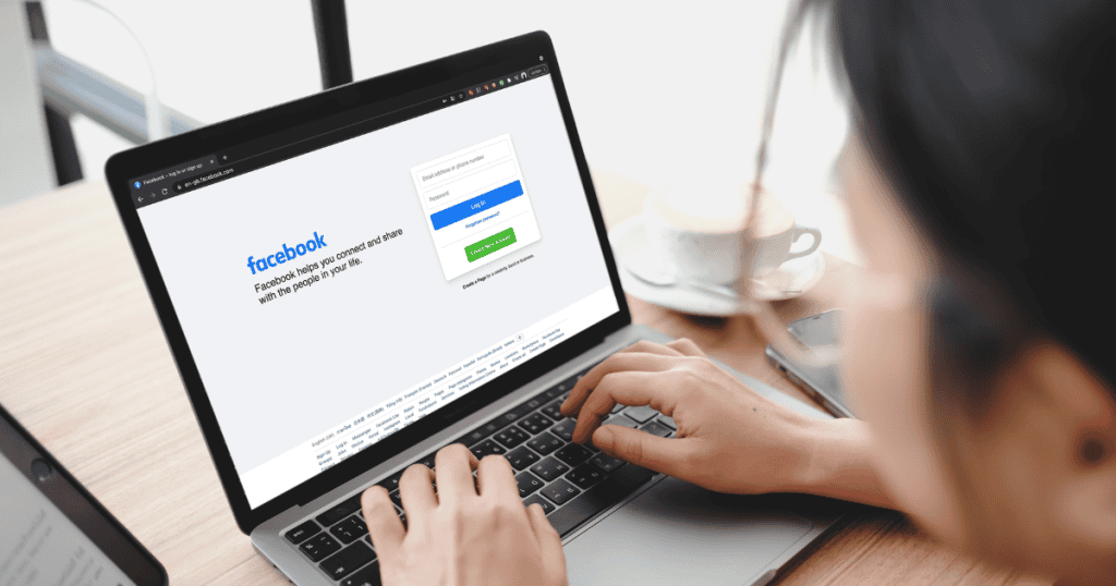 An over-the-shoulder view of a woman looking at a laptop displaying the Facebook login page, capturing the initial step in crafting a social media presence.