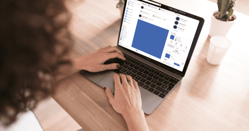 A woman with curly hair types on a laptop at a wooden desk, her focus directed toward an active social media profile on the screen.